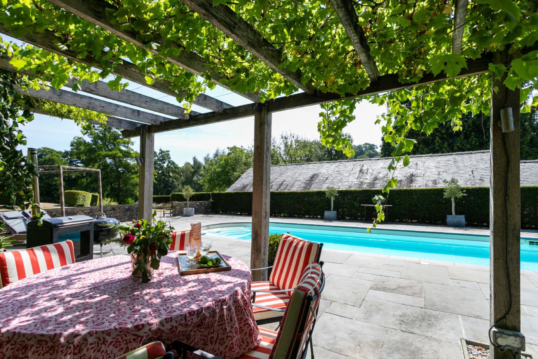 The poolside dining table at Swallow's Cottage, striped cushions in the summer sun
