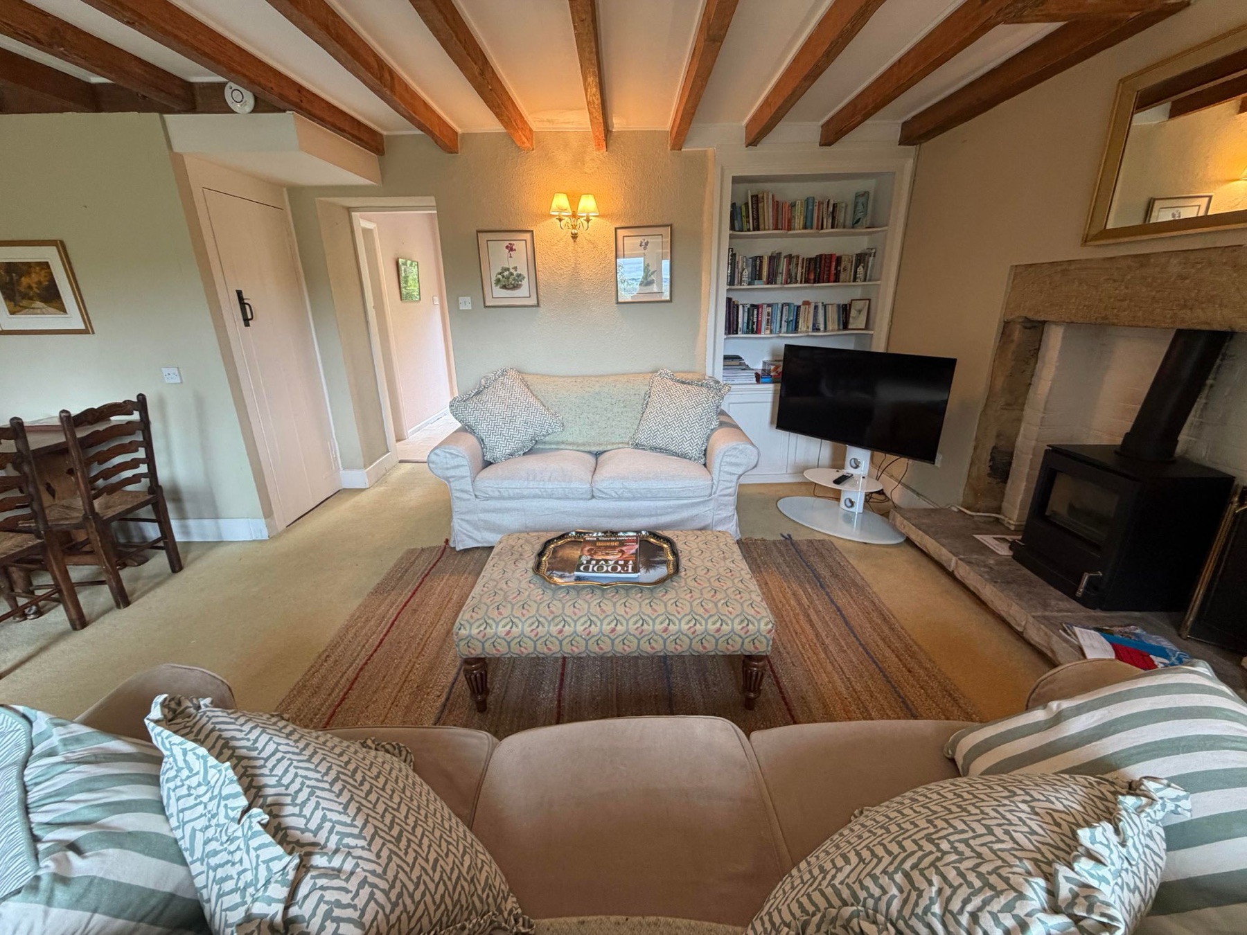 The sitting room at Woodside Cottage, sofas around the footstool and log burning stove, bookshelves behind