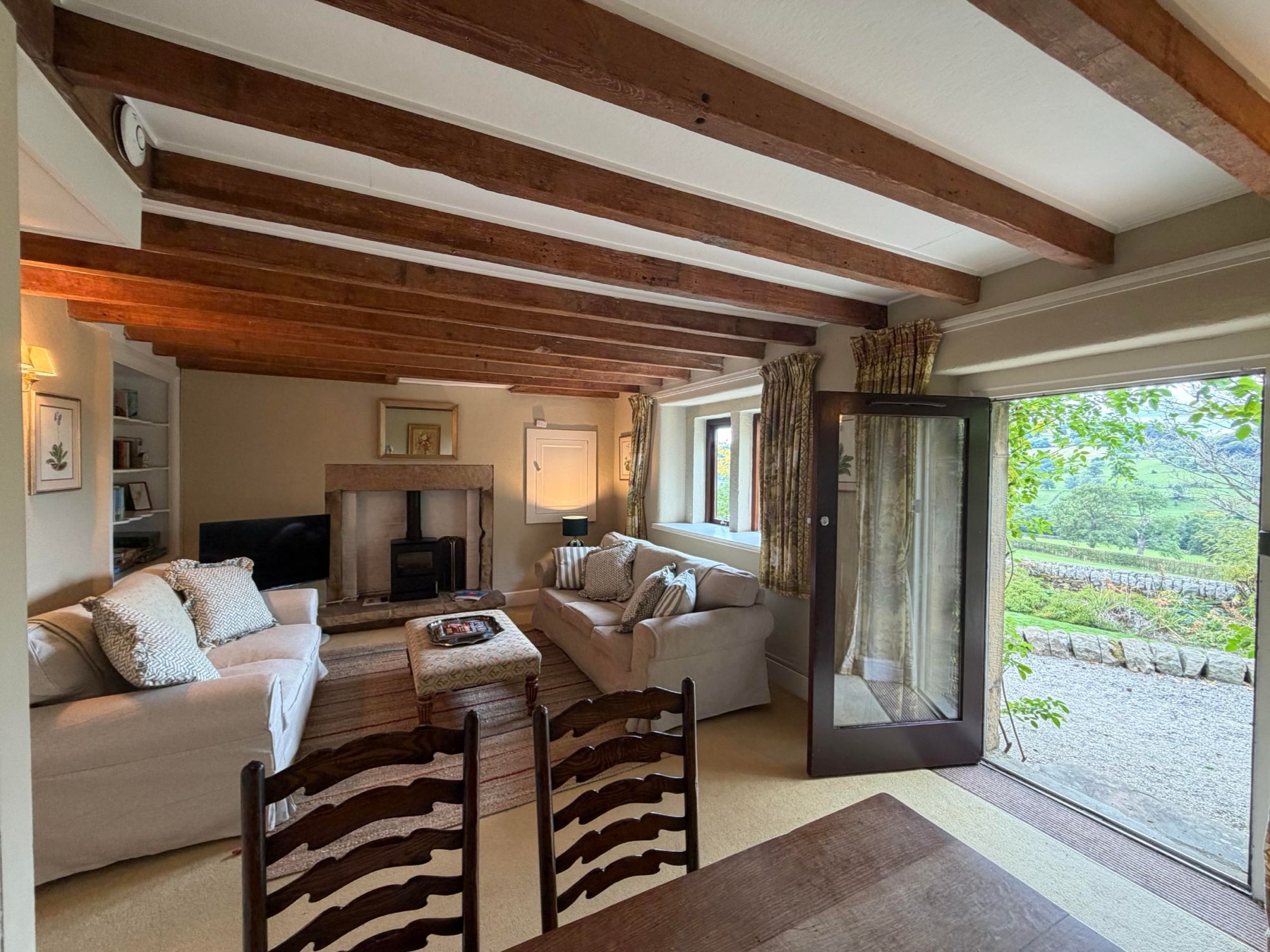 The beamed sitting room at Woodside Cottage, log burning stove and the door open onto the valley
